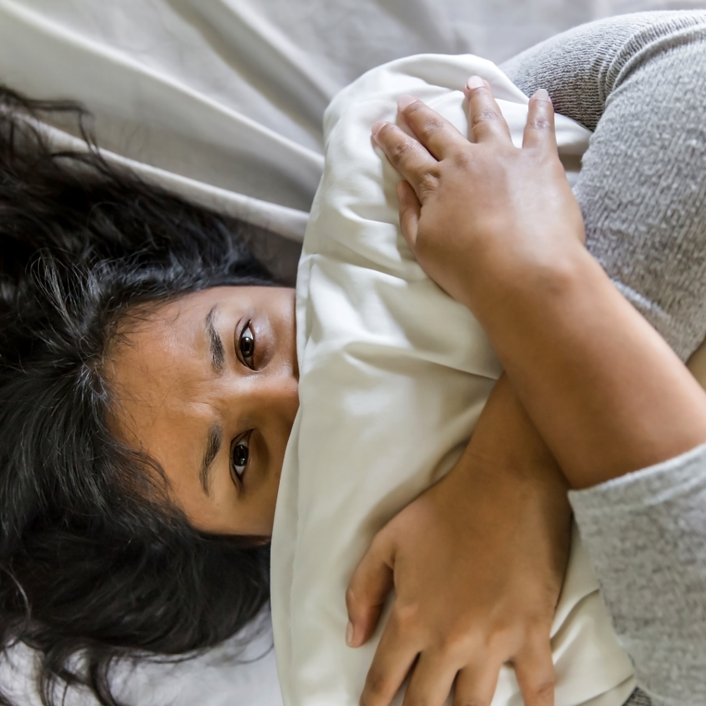 Woman in bed with pillow over her mouth because she is struggling with panic attack