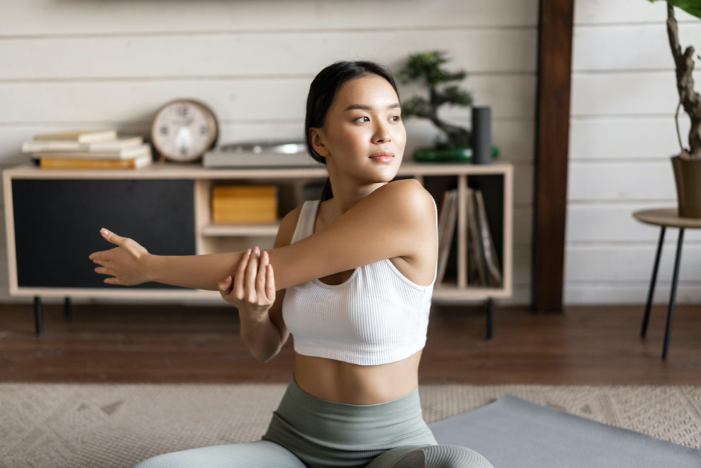 Asian fitness girl doing workout at home sitting on floor mat in activewear warm up 