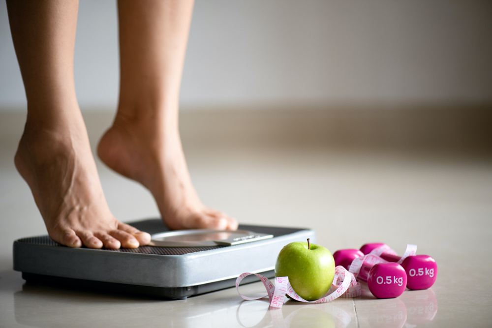 Female leg stepping on weigh scales with measuring tape