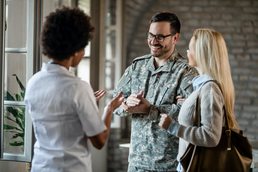 Happy army soldier and his wife communicating with african american healthcare worker while having consultations at the doctors office.