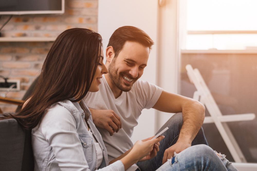 happy couple enjoying media content in a smart phone sitting on the floor
