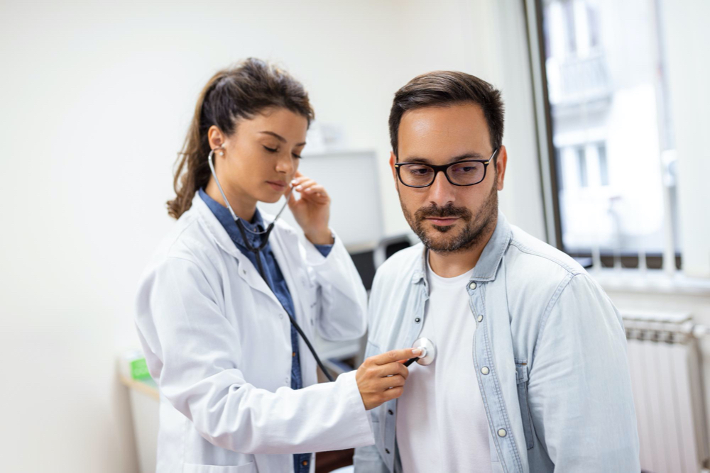 photo caring caucasian female doctor use phonendoscope examine male patient heart rate at consultation in hospital 