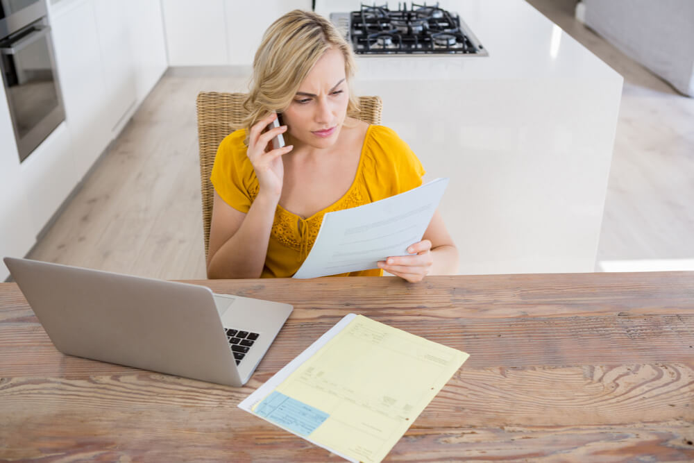 Woman talking on mobile phone while looking at lab work in kitchen
