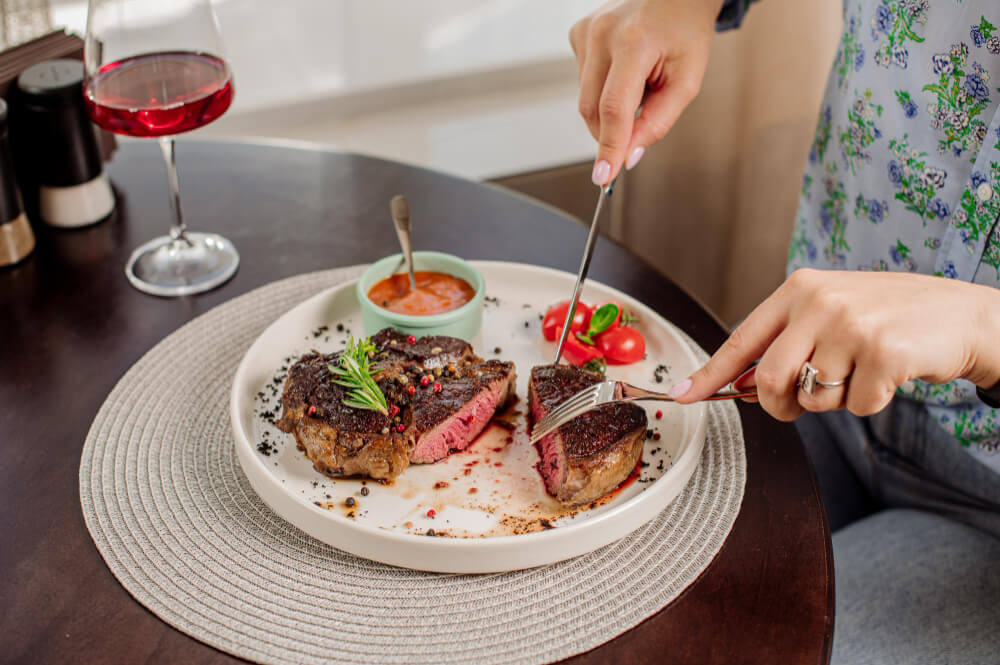 Woman client of the restaurant is eating a medium rare steak Close up
