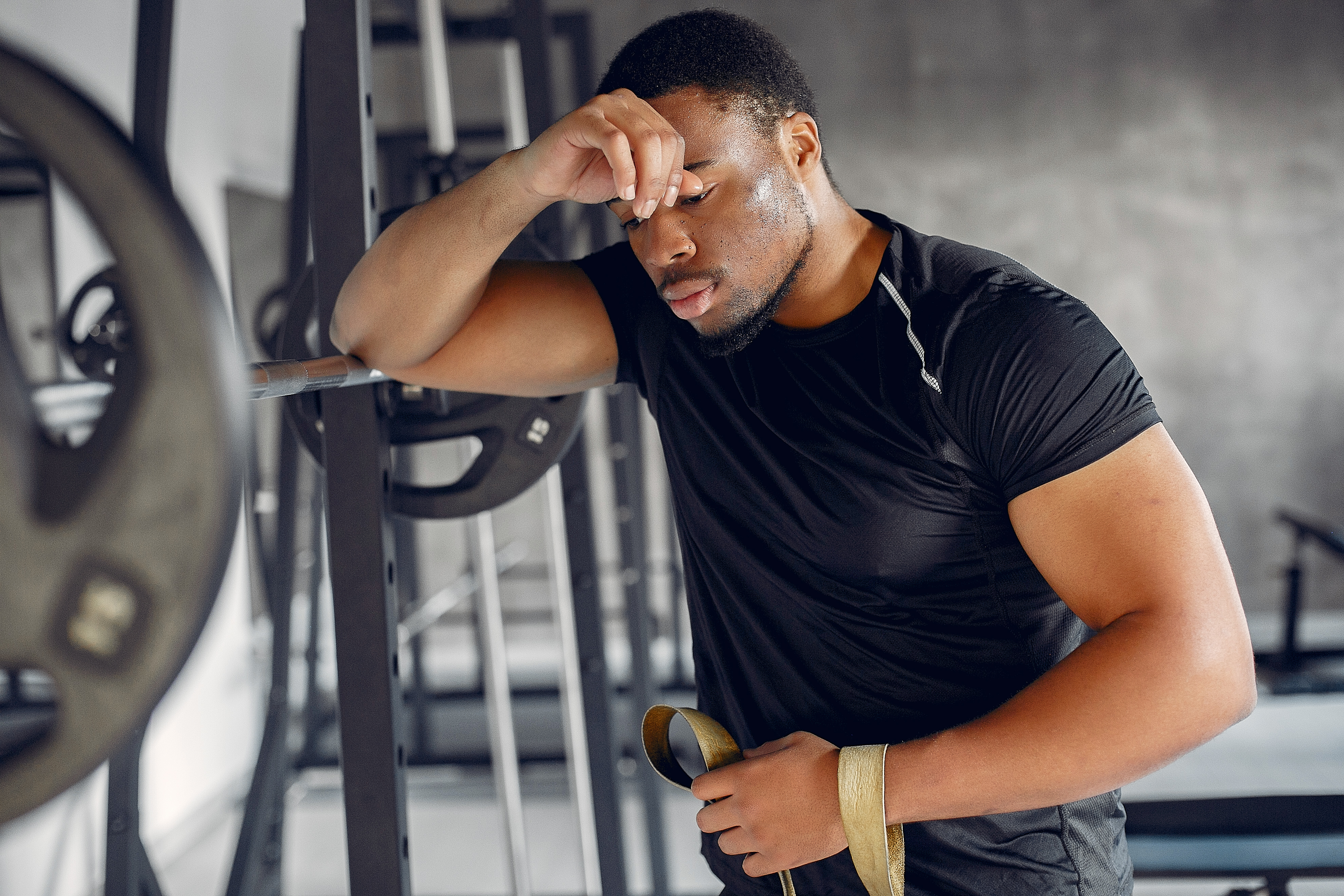 Exhausted athlete recovering after intense exercise in a gym, illustrating overtraining symptoms, workout fatigue, and the need for proper recovery.