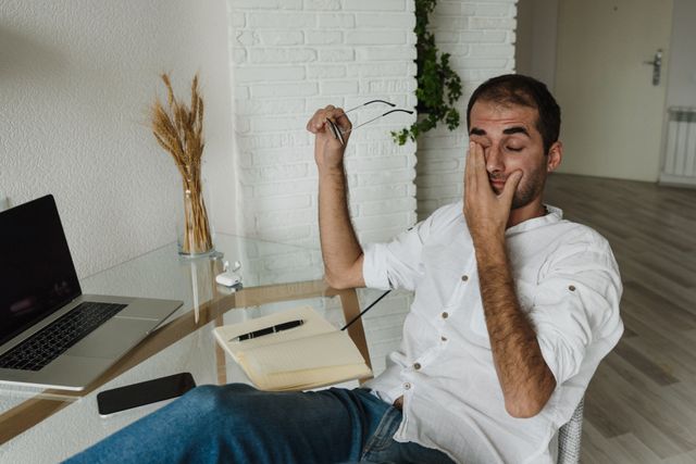 Tired woman sitting at desk in the morning rubbing her eyes, showing signs of chronic fatigue
