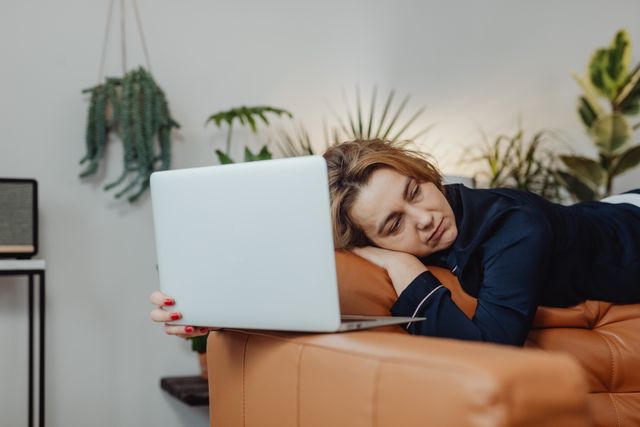 Tired woman sitting at desk in the morning rubbing her eyes, showing signs of chronic fatigue